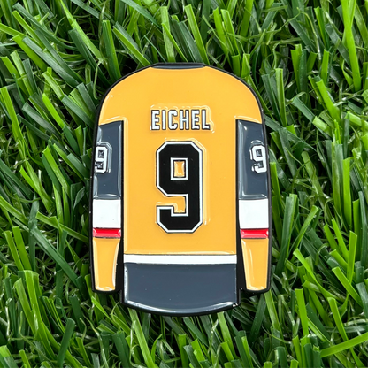 Jack Eichel golf ball marker featuring a yellow and black jersey design with number 9, placed on green grass.