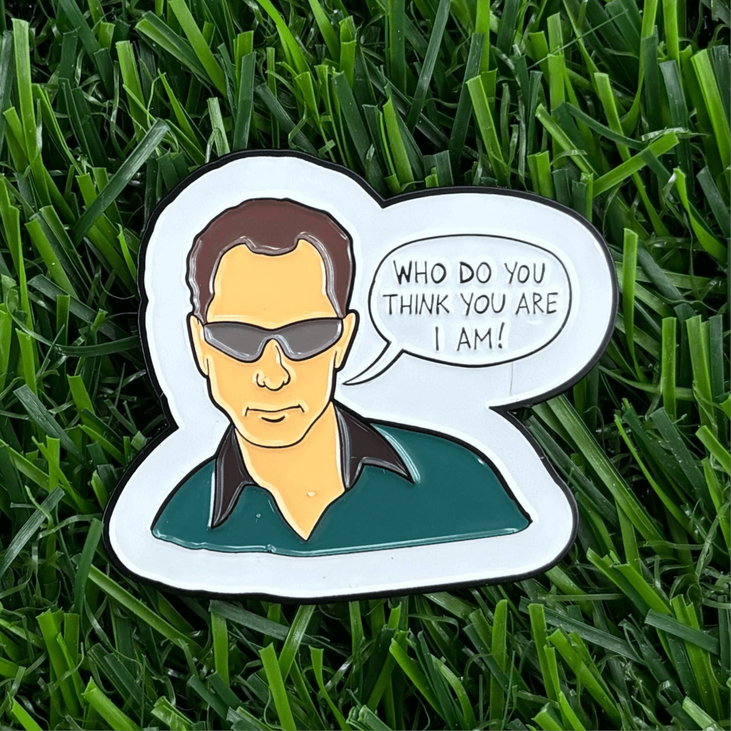 "Who Do You Think You Are I Am" golf ball marker featuring stylized design on green grass, a unique and durable golfing accessory