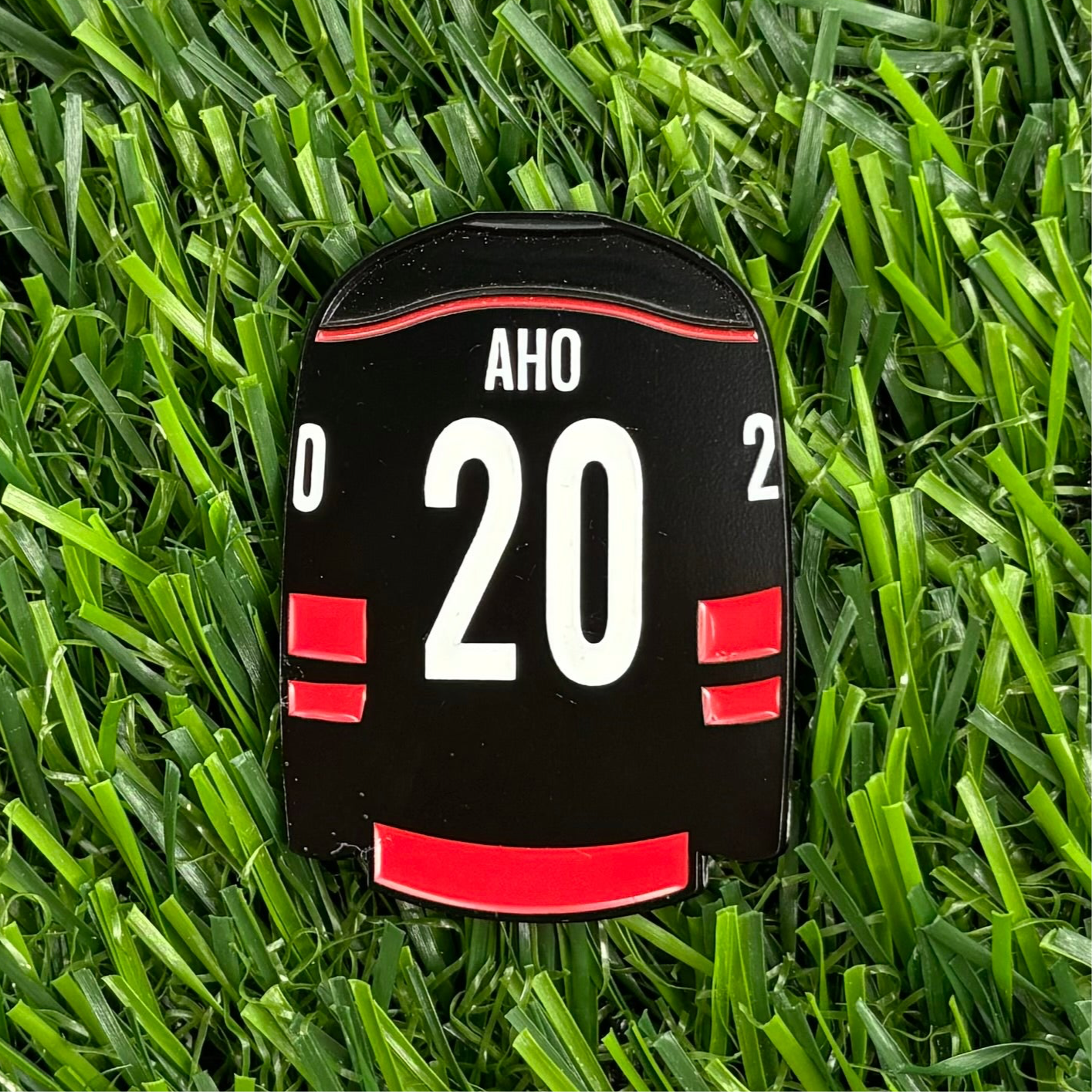 Sebastian Aho golf ball marker designed to resemble a sports jersey featuring number 20 lying on grass.