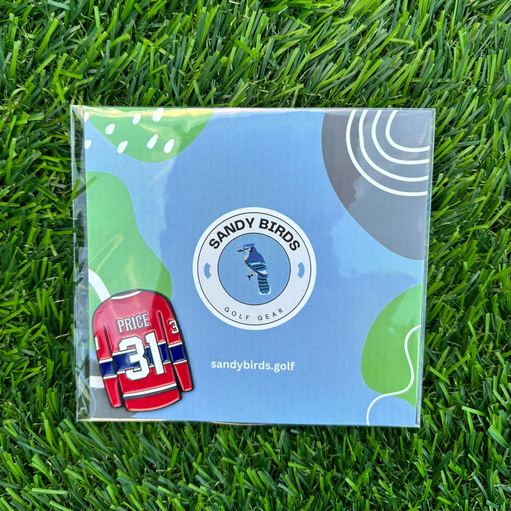 Carey Price custom golf ball marker on grass with Sandy Birds packaging.