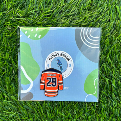 Leon Draisaitl golf ball marker on grass, featuring jersey design and included with Sandy Birds packaging.