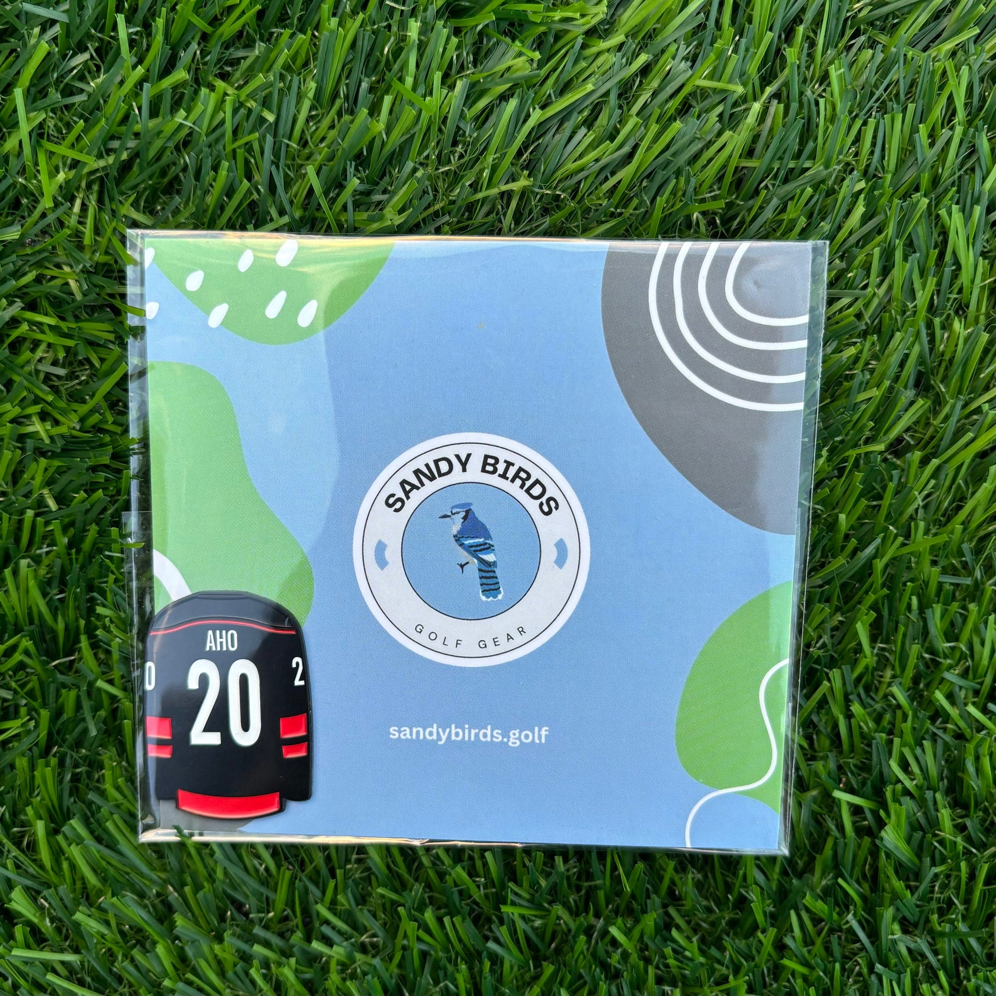 Sebastian Aho custom golf ball marker by Sandy Birds, featuring a unique design, displayed on green grass.