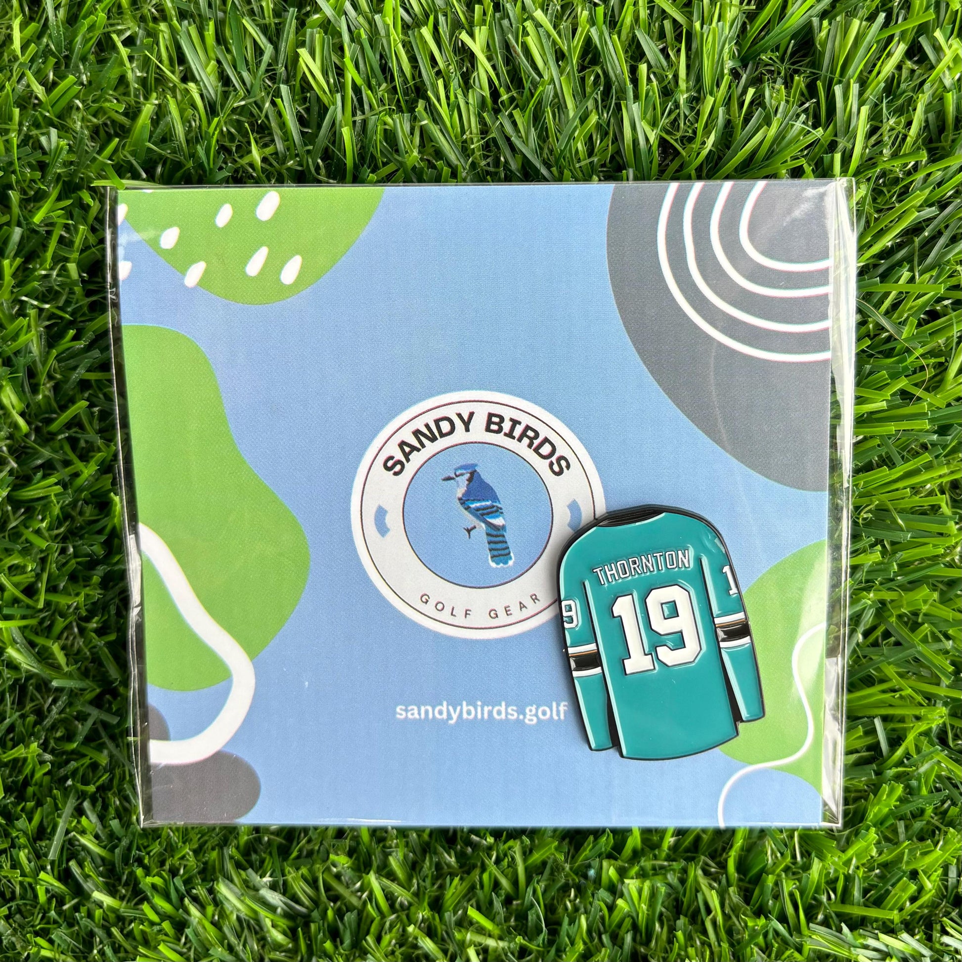 Joe Thornton golf ball marker set on grass with Sandy Birds logo