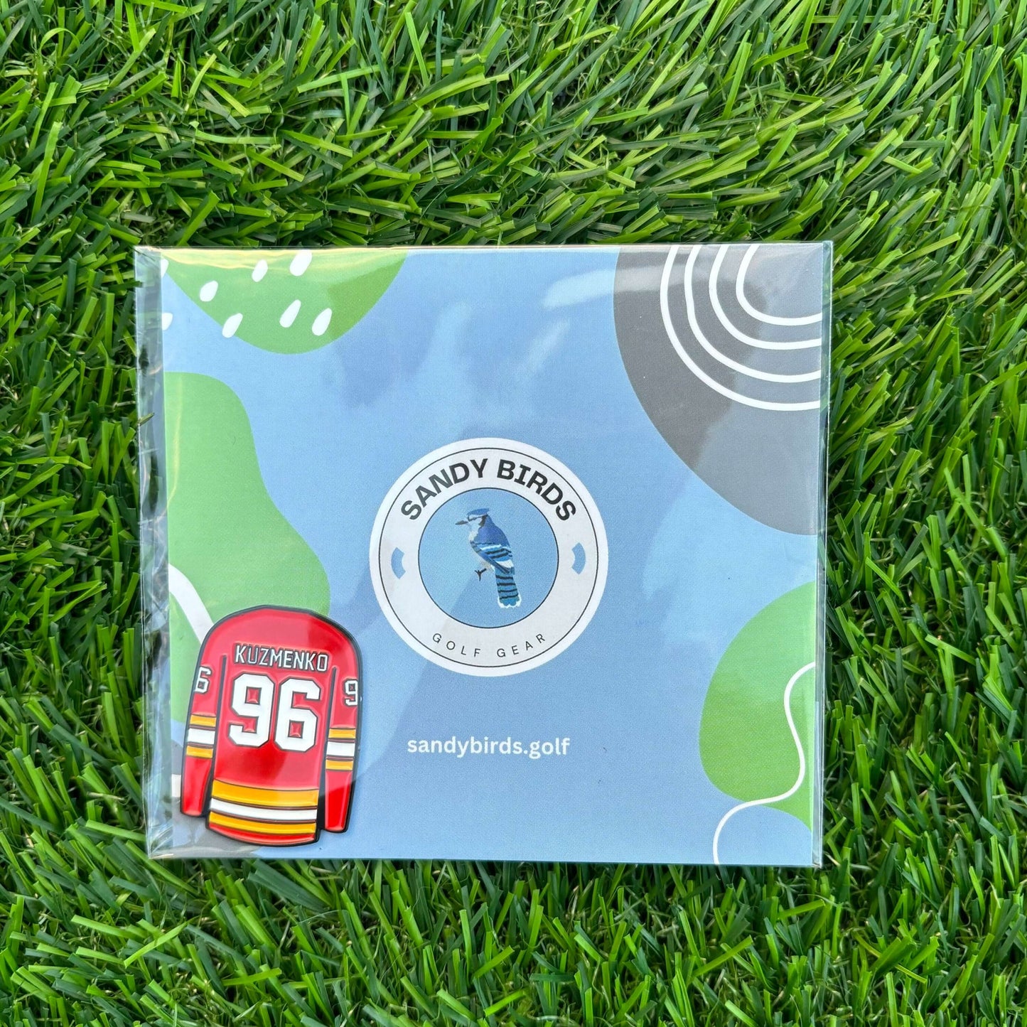 Andrei Kuzmenko golf ball marker in Sandy Birds packaging on grass