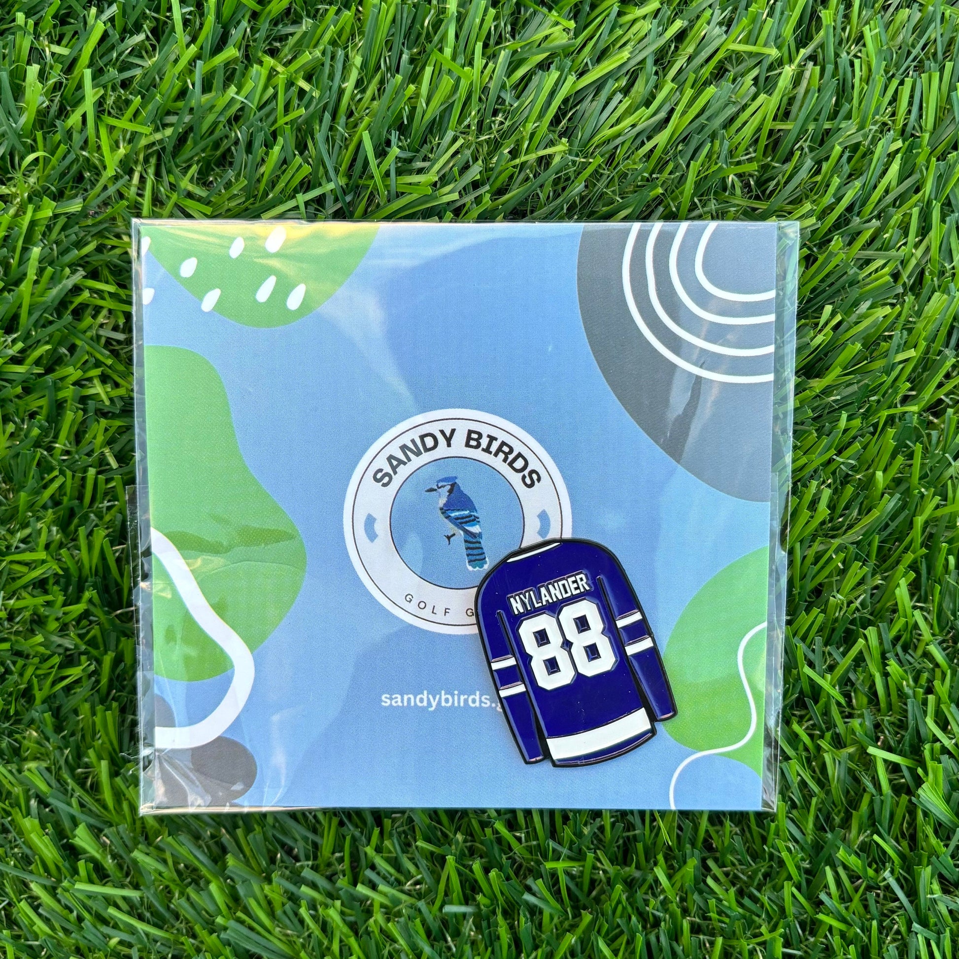 William Nylander custom golf ball marker on grass with Sandy Birds logo packaging