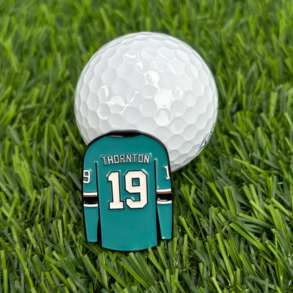 Joe Thornton golf ball marker with turquoise jersey design and white golf ball on grass