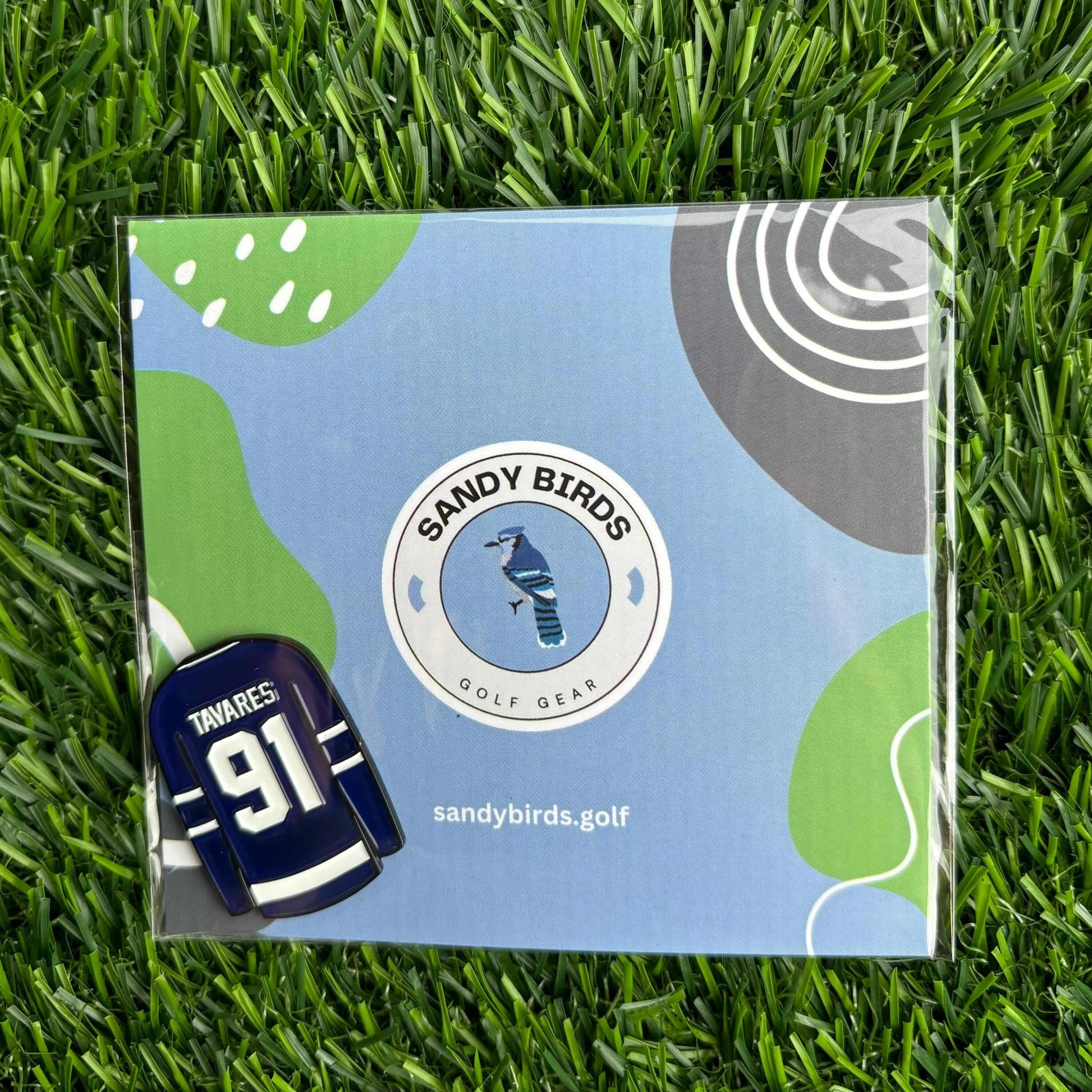 John Tavares golf ball marker by Sandy Birds on grass, packaged with stylish golf-themed background